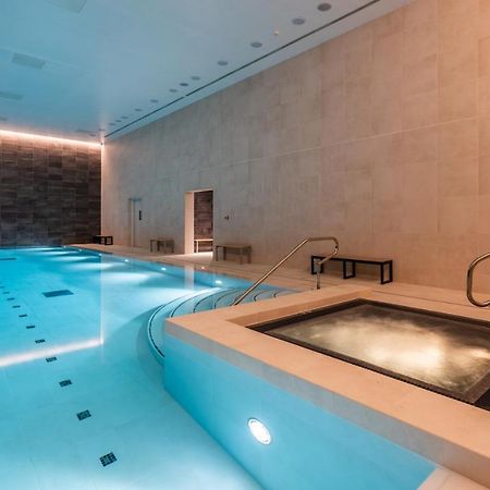 Citysuites 2 Aparthotel Manchester Exteriér fotografie The photo shows an indoor swimming pool area. The pool is a bright blue color and features smooth, tiled surfaces. On one side, there is a hot tub area with steps leading into it. The walls are made of light-colored stone, and there is ambient lighti