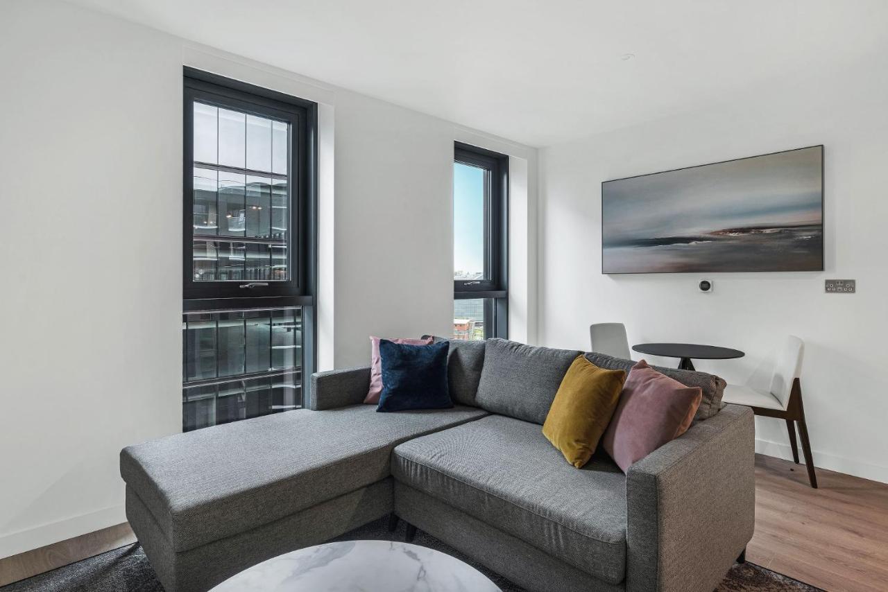 Citysuites 2 Aparthotel Manchester Exteriér fotografie The photo shows a modern living space featuring a gray sectional sofa adorned with colorful throw pillows. There are large windows allowing natural light to fill the room, offering a view of the outdoors. A wall-mounted television is positioned above