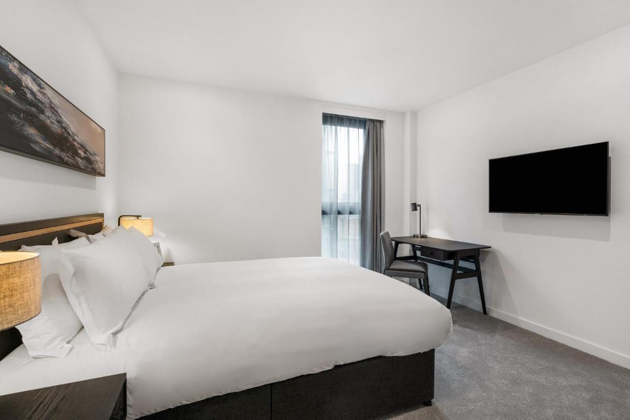 Citysuites 2 Aparthotel Manchester Exteriér fotografie The photo shows a modern hotel room featuring a large bed with white linens and a dark headboard. There are two bedside lamps on either side of the bed. A desk with a chair is placed against one wall, and a flat-screen TV is mounted on another wall. 