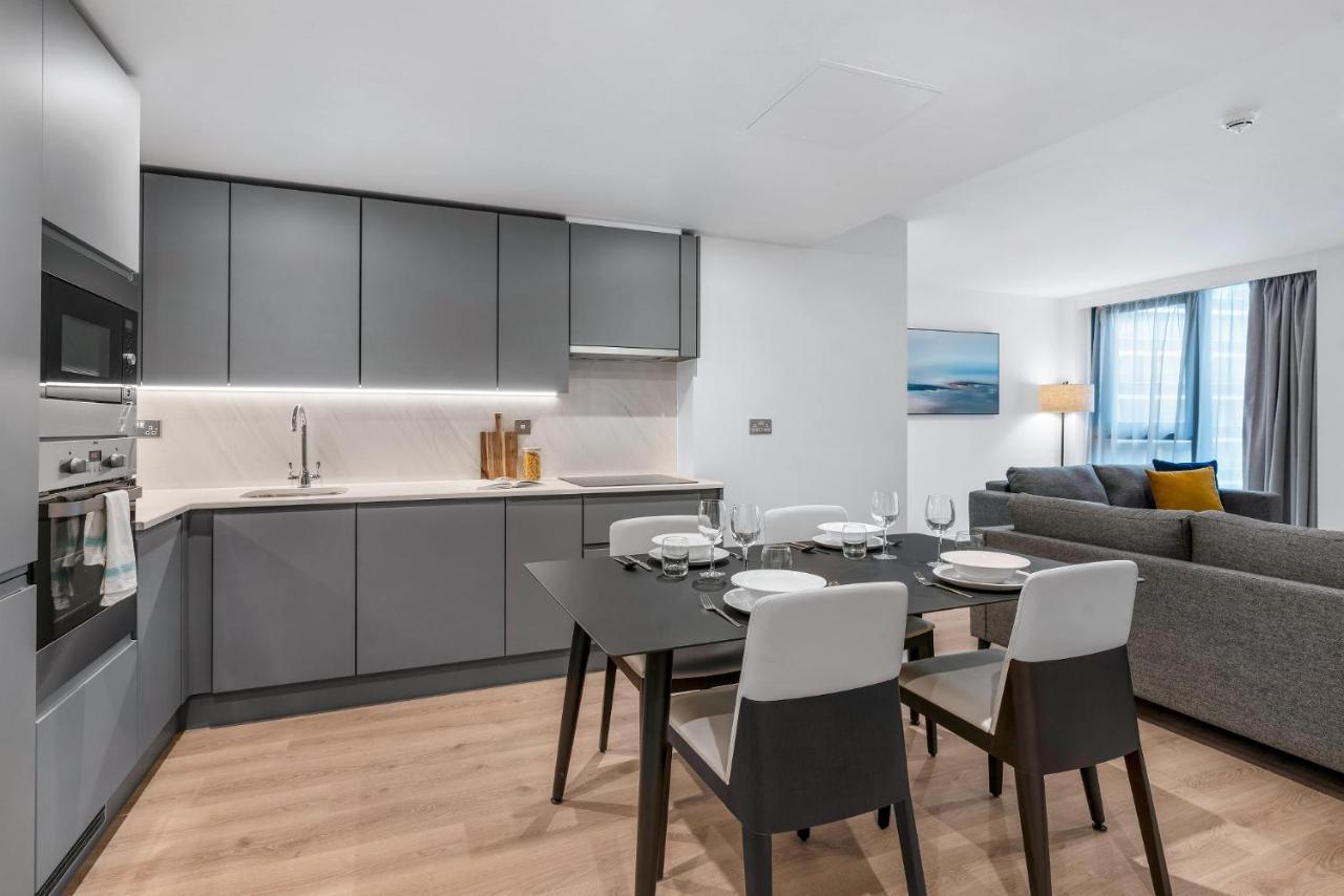 Citysuites 2 Aparthotel Manchester Exteriér fotografie The photo shows a modern, open-concept kitchen and living area. The kitchen features sleek, gray cabinetry with a countertop, a sink, and built-in appliances. There are cooking utensils displayed on the countertop. Next to the kitchen, there is a din