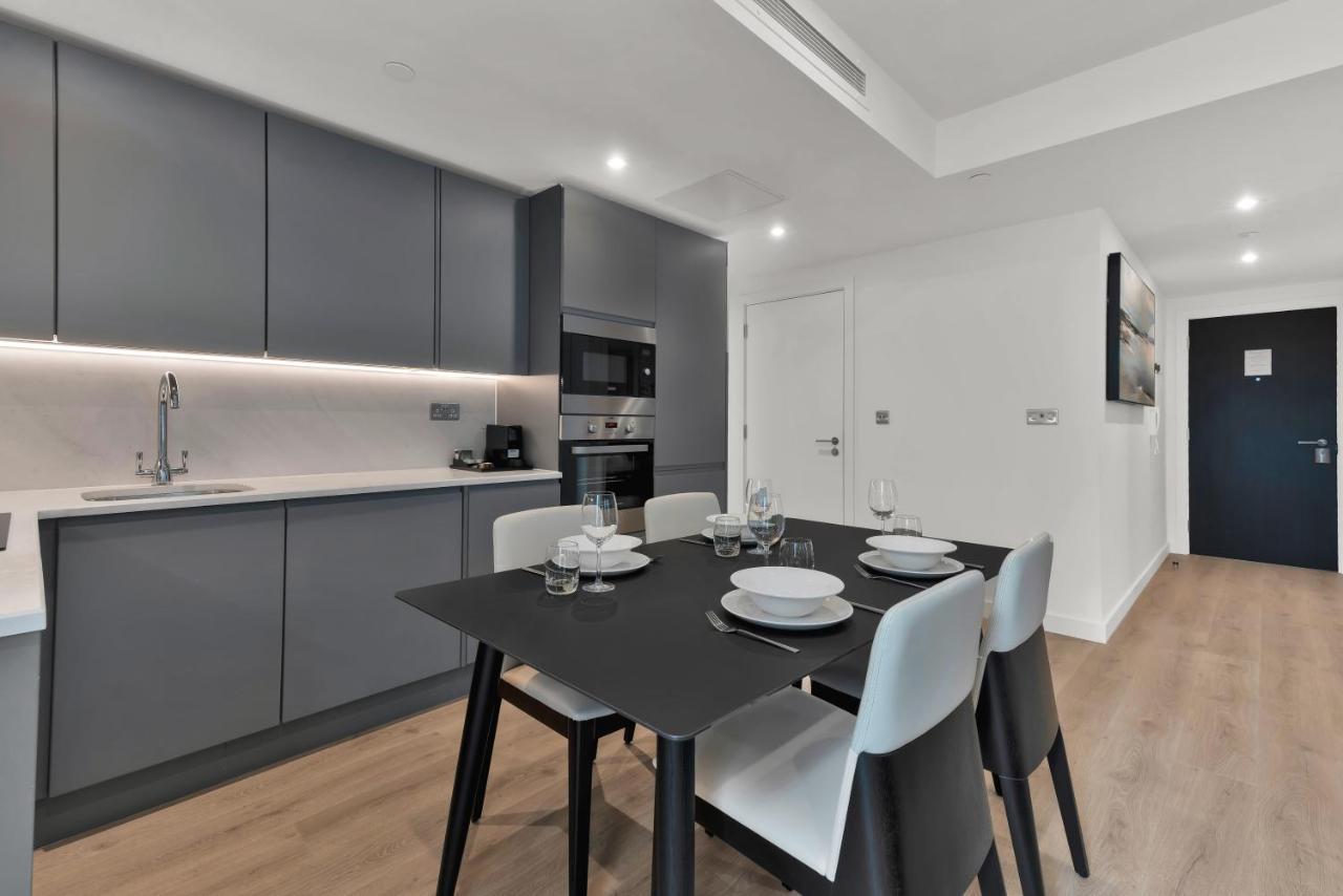 Citysuites 2 Aparthotel Manchester Exteriér fotografie The photo shows a modern kitchen and dining area. There are sleek gray cabinetry and countertops, with a built-in oven and microwave. The kitchen is well-lit, featuring under-cabinet lighting that adds to the contemporary feel. In the dining area, th