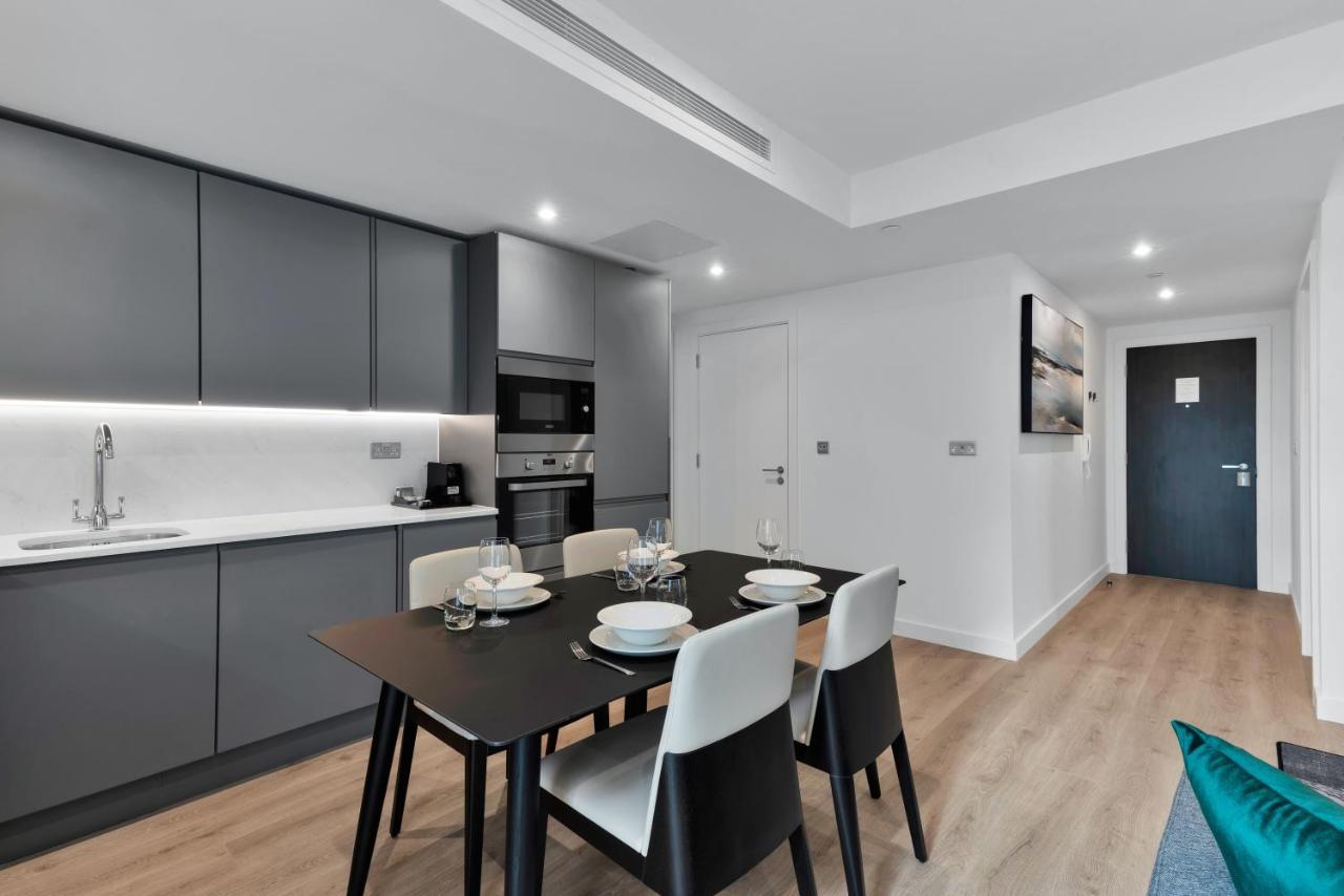 Citysuites 2 Aparthotel Manchester Exteriér fotografie The image shows a modern kitchen and dining area. The kitchen features sleek gray cabinets with a white countertop, and it is equipped with appliances such as a microwave. There’s a dining table set for four, with white plates and glasses ready. The 