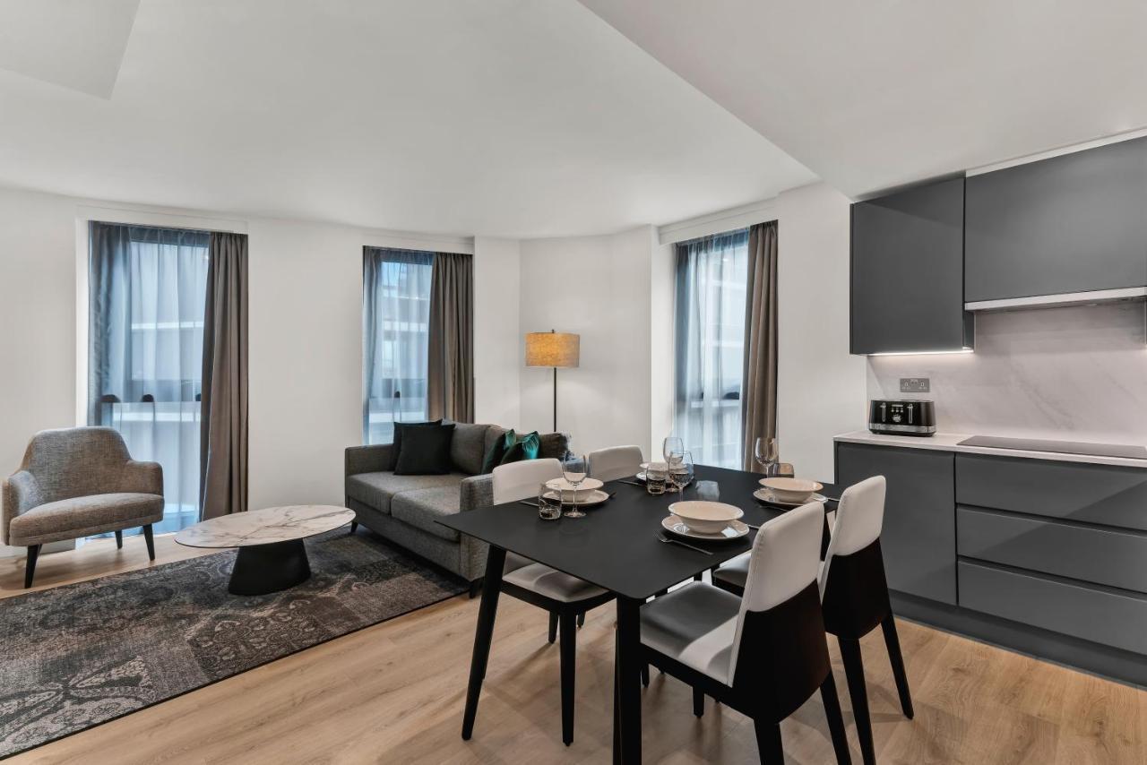 Citysuites 2 Aparthotel Manchester Exteriér fotografie The photo shows a modern living space that includes a dining area and a seating area. There's a sleek black dining table set with plates and cutlery, accompanied by white and black chairs. To one side, a comfortable gray sofa faces the dining area, c