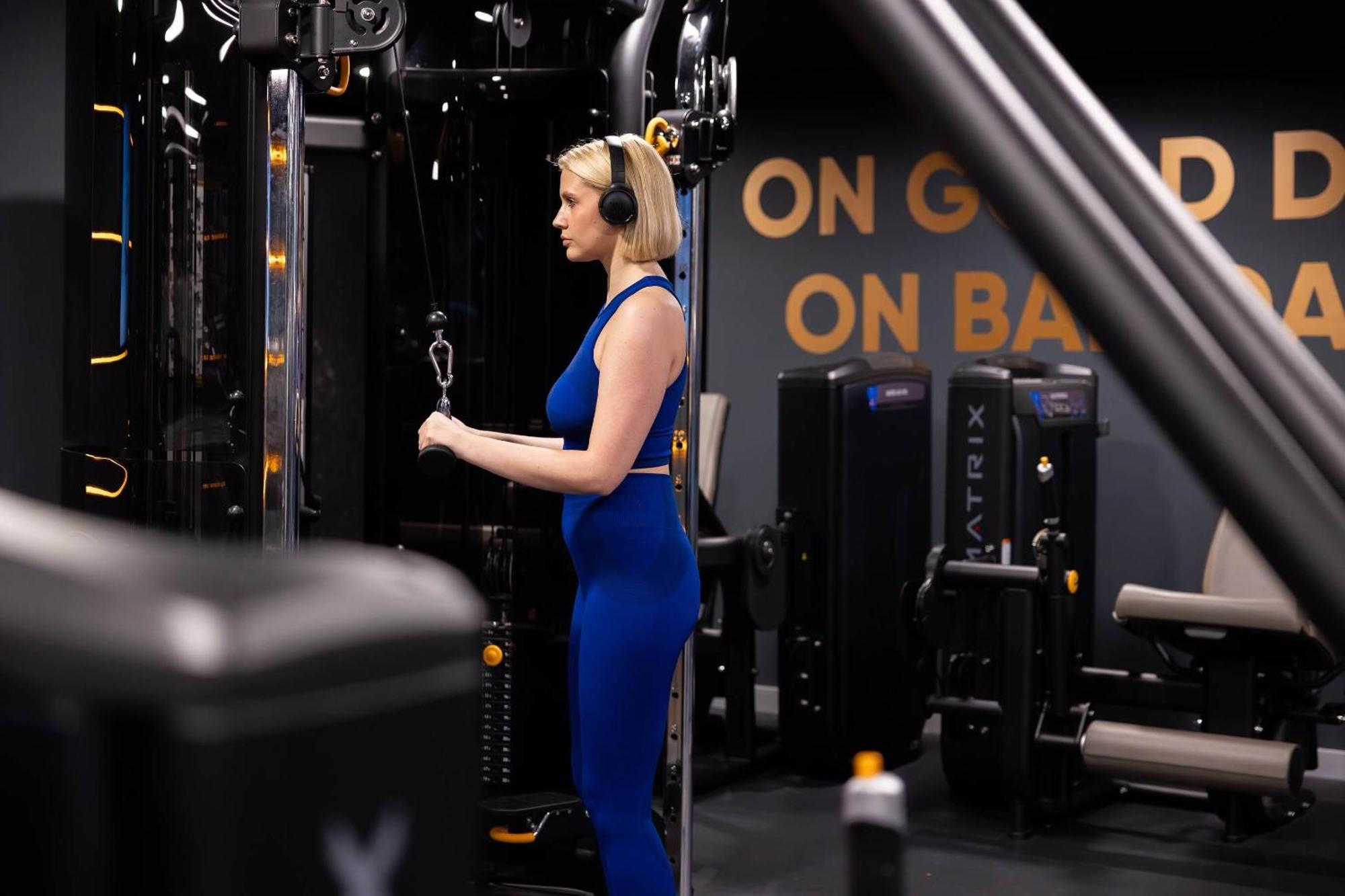 Citysuites 2 Aparthotel Manchester Exteriér fotografie The photo shows a woman working out in a gym. She is wearing a blue athletic outfit and headphones while using a gym machine. The background features various other gym equipment and a wall with the words "ON GOOD ON BAD" displayed prominently. The se