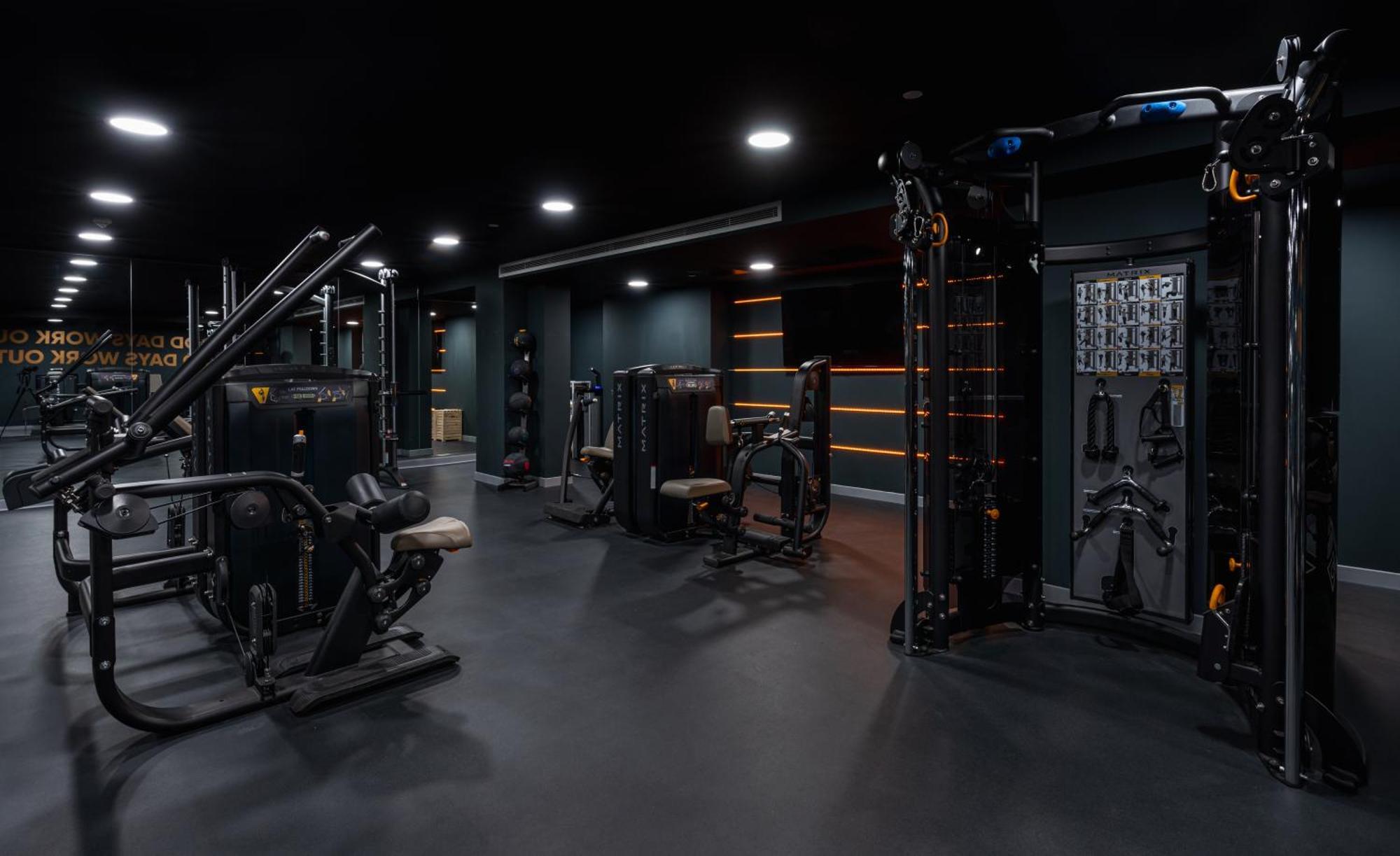 Citysuites 2 Aparthotel Manchester Exteriér fotografie The photo shows a modern gym or fitness area with various workout machines. The space has a dark color scheme, featuring black walls and flooring. There are multiple pieces of exercise equipment, including stations for strength training, possibly tar