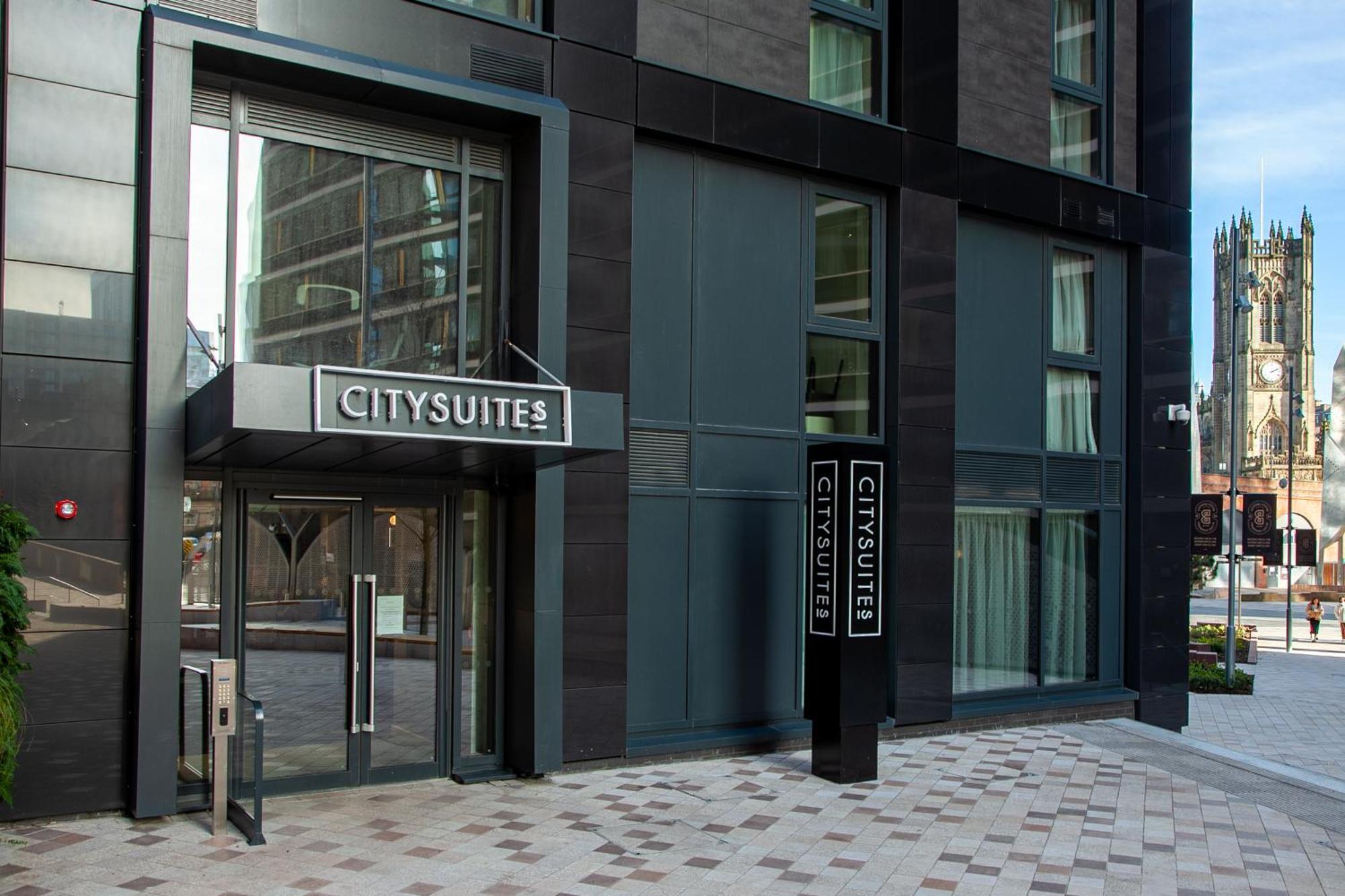 Citysuites 2 Aparthotel Manchester Exteriér fotografie The photo shows the entrance to a modern building labeled "CITYSUITES." The entrance features large glass doors and a sleek, contemporary design. The building has dark exterior panels and large windows, suggesting a stylish and urban environment. The