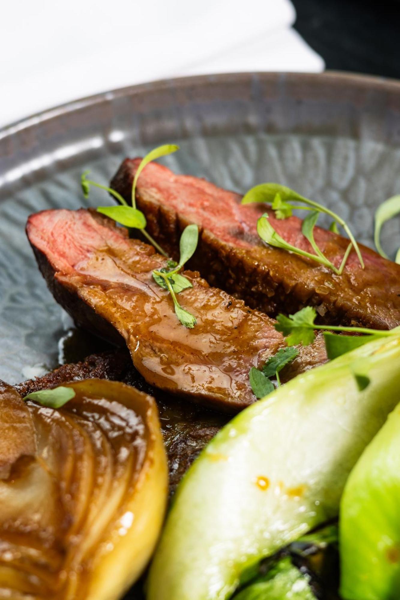 Citysuites 2 Aparthotel Manchester Exteriér fotografie The photo features slices of meat, likely beef, presented on a decorative plate. The meat appears to have a rich brown sauce drizzled over it and is garnished with fresh herbs, adding a pop of green. There are also some slices of a light-colored vege