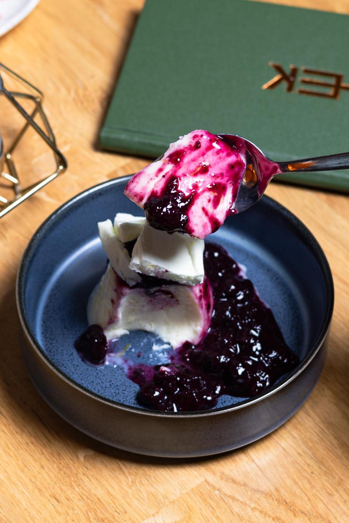 Citysuites 2 Aparthotel Manchester Exteriér fotografie The photo shows a serving of dessert, likely a type of panna cotta or a creamy custard, partially dished out and accompanied by a rich berry sauce, possibly made from blueberries or blackberries. A spoon with some of the dessert and sauce is hovering